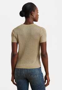 Sweater de malha canelada de manga curta em dourado claro com um design ajustado. Costas lisas e decote redondo, combinado com jeans azul escuro.