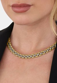 Collar de cadena de oro y plata con eslabones entrelazados, que presenta una textura suave y un acabado brillante, llevado sobre una prenda oscura.