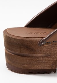 Brown leather platform sandal with a textured wood heel, featuring a smooth footbed and minimal stitching details.