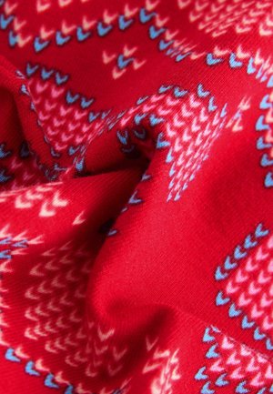 Rød stof med et geometrisk mønster i blå, pink og hvide nuancer. Teksturen er blød og en smule strækbar.