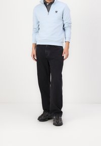 Felpa blu chiaro con zip e colletto grigio, abbinata a jeans neri a gamba dritta e scarpe da ginnastica nere con suole testurizzate.