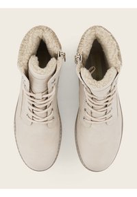 Bottes d'hiver beiges avec devant à lacets et doublure intérieure en molleton doux, vues de dessus sur un fond clair.