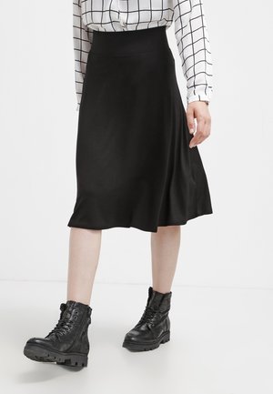 Jupe noire en A en tissu lisse, dotée d'une taille haute et d'une silhouette fluide, associée à des bottes de combat noires à lacets.