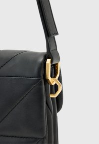 Czarna skórzana torebka z pikowanym wzorem, z złotą geometryczną klamrą i usztywnianym paskiem do noszenia.