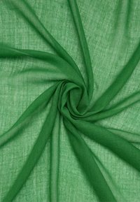 Zielony przezroczysty materiał o lekko teksturowanej powierzchni, ułożony w spiralę, ukazujący jego lekkość i przewiewność.