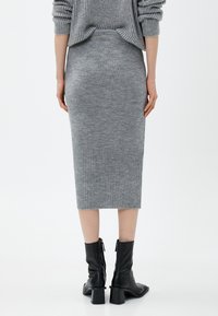 Hame grey ribbed dengan bentuk fit, menampilkan hem bawah yang berpola tekstur. Dipasangkan dengan sepatu bot pergelangan kaki hitam dengan hak tebal.
