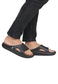 Des sandales noires en caoutchouc moulé avec une semelle contour, présentant deux sections découpées et un logo discret sur le côté.