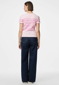 Ružičasti prugasti rebrasti džemper s valovitim rukavima, uparen s tamnoplavim trapericama visokog struka i širokih nogavica.