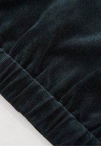 Gros plan sur un tissu en velours côtelé vert foncé avec une texture côtelée visible et une ceinture élastique froncée sur un vêtement.