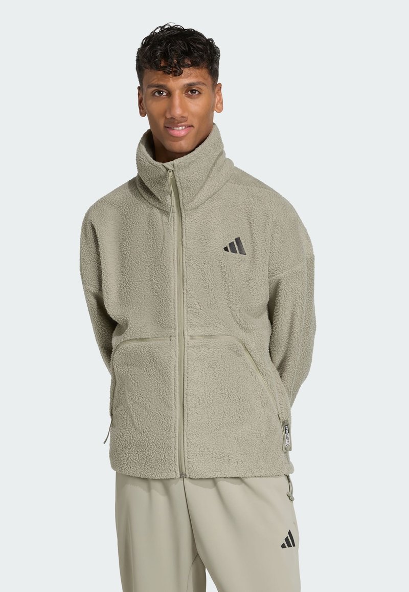 Light green fleece jacket with a high collar, full zipper, and two front pockets. Features black logo detailing on the chest.