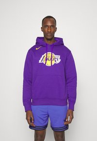 Felpa viola con logo dei Los Angeles Lakers, tasca a marsupio e swoosh Nike. Abbinata a pantaloni corti in mesh blu con strisce nere.