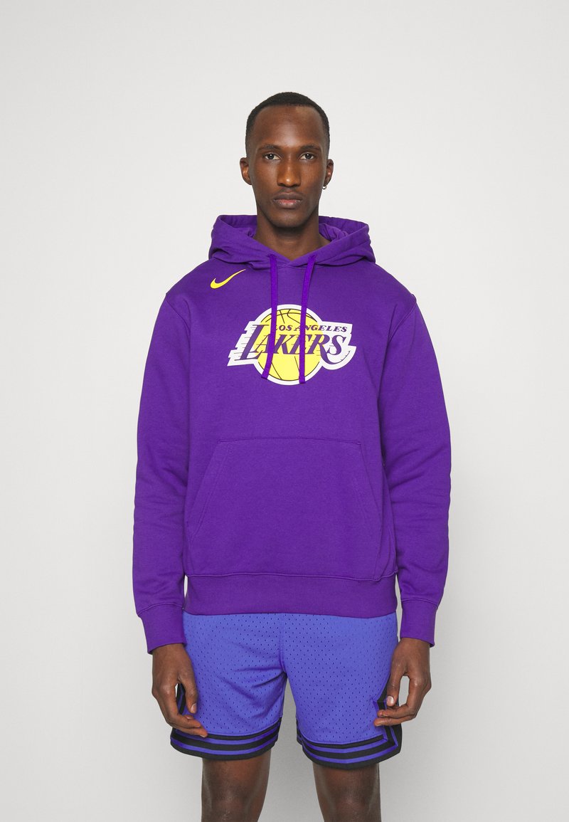 Felpa viola con logo dei Los Angeles Lakers, tasca a marsupio e swoosh Nike. Abbinata a pantaloni corti in mesh blu con strisce nere.