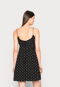 Vestido preto floral com alças finas ajustáveis, decote franzido e corpete justo, apresentando um fecho a laço nas costas.