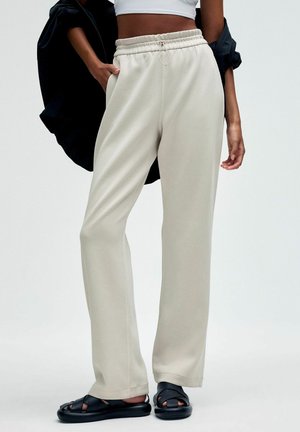 Beige, weit geschnittene Hosen mit einem elastischen Bund und Kordelzug. Hergestellt aus einem weichen, glatten Stoff. Kombiniert mit schwarzen Riemchensandalen.