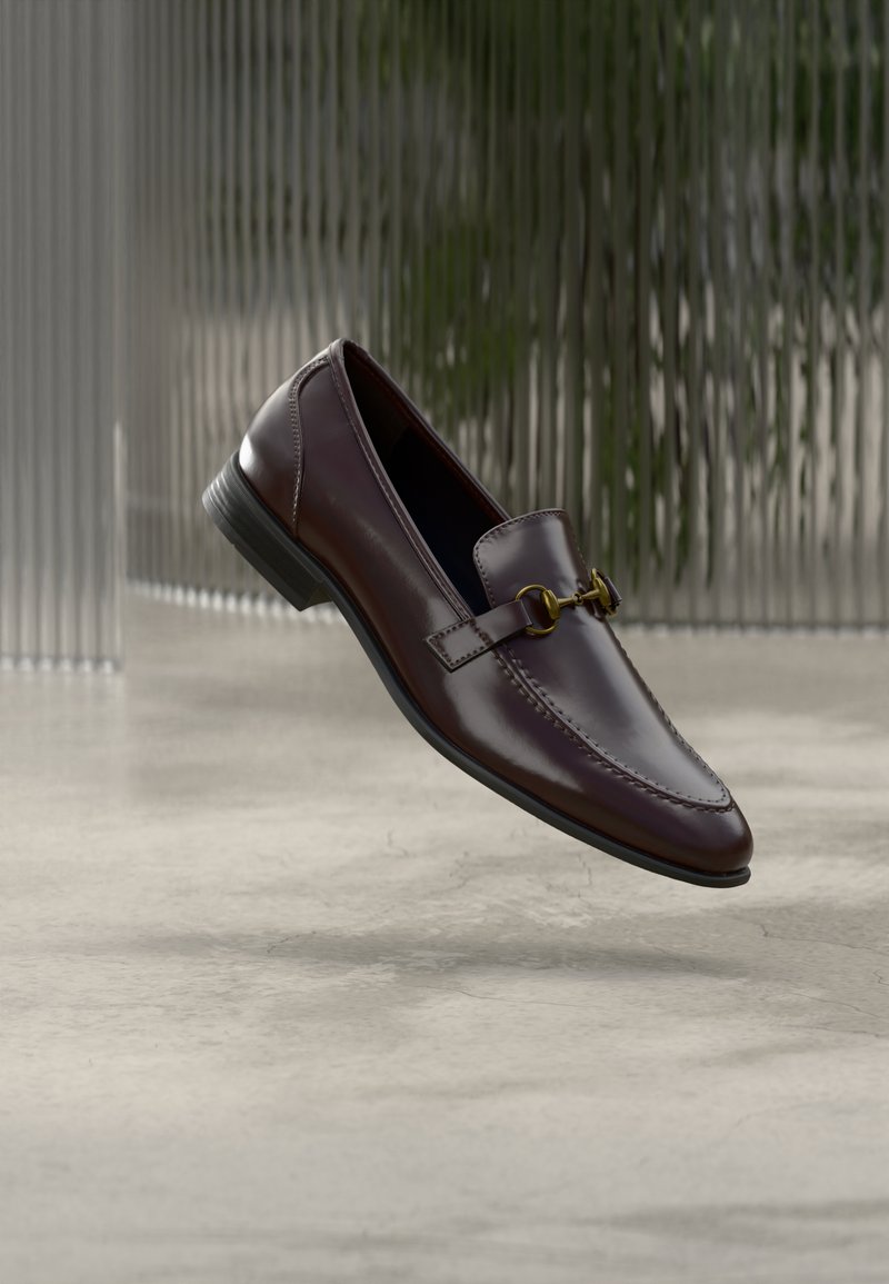 Mocassin en cuir marron à finition lisse, bout carré, et accent en métal doré. Dispose d'un talon bas et de détails de couture subtils.