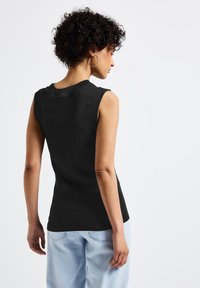 Top nero senza maniche con un design a costine testurizzato e scollo a barca, abbinato a jeans blu chiaro dal taglio morbido.