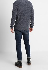 Granatowy sweter o teksturowanym splocie z okrągłym dekoltem, w połączeniu z dopasowanymi ciemnoniebieskimi dżinsami i czarnymi botkami za kostkę z brązową podeszwą.