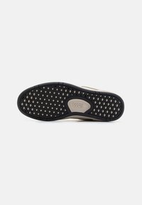 Vans Schuhsohle, schwarzes Gummi mit einem strukturierten Muster, ausgestattet mit einer beigen Zwischensohle und Logodetails. Glatte und langlebige Oberfläche.