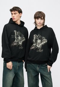 Juodi gobtuvai su dideliu baltu drugelio grafiniu ir teksto dizainu priekyje. Laisvo stiliaus, su kengūros kišene ir raišteliais.