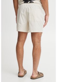 Beige swim shorts with an elastic waistband, featuring a rear patch pocket and a lightweight, soft fabric texture.