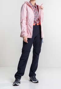 Vaaleanpunainen vedenpitävä takki, kukallinen paita, tummansiniset vetoketjulliset cargo-housut ja mustat tennarit valkoisilla yksityiskohdilla. Kuminauhakupeilla ja säädettävillä ominaisuuksilla.