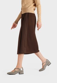 Scarpe in pelle lucida grigia con design a T, tacco blocco basso e dettagli a taglio. Indossate con un cardigan beige e una gonna marrone.