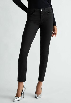 Strakke zwarte broek met gestuddede voorzakken, gedragen met zilveren hoge hakken en een zwart topje met lange mouwen.