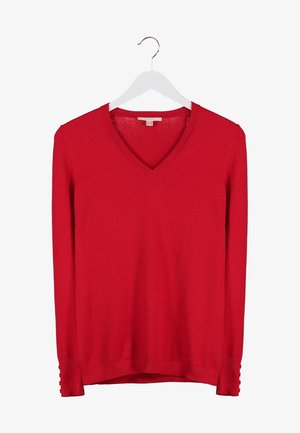 Czerwony sweter w serek z długimi rękawami, zestawiony z ciemnoniebieskimi rurkami i czarnymi botkami za kostkę. Mała czarna torebka na ramię z łańcuszkowym paskiem.