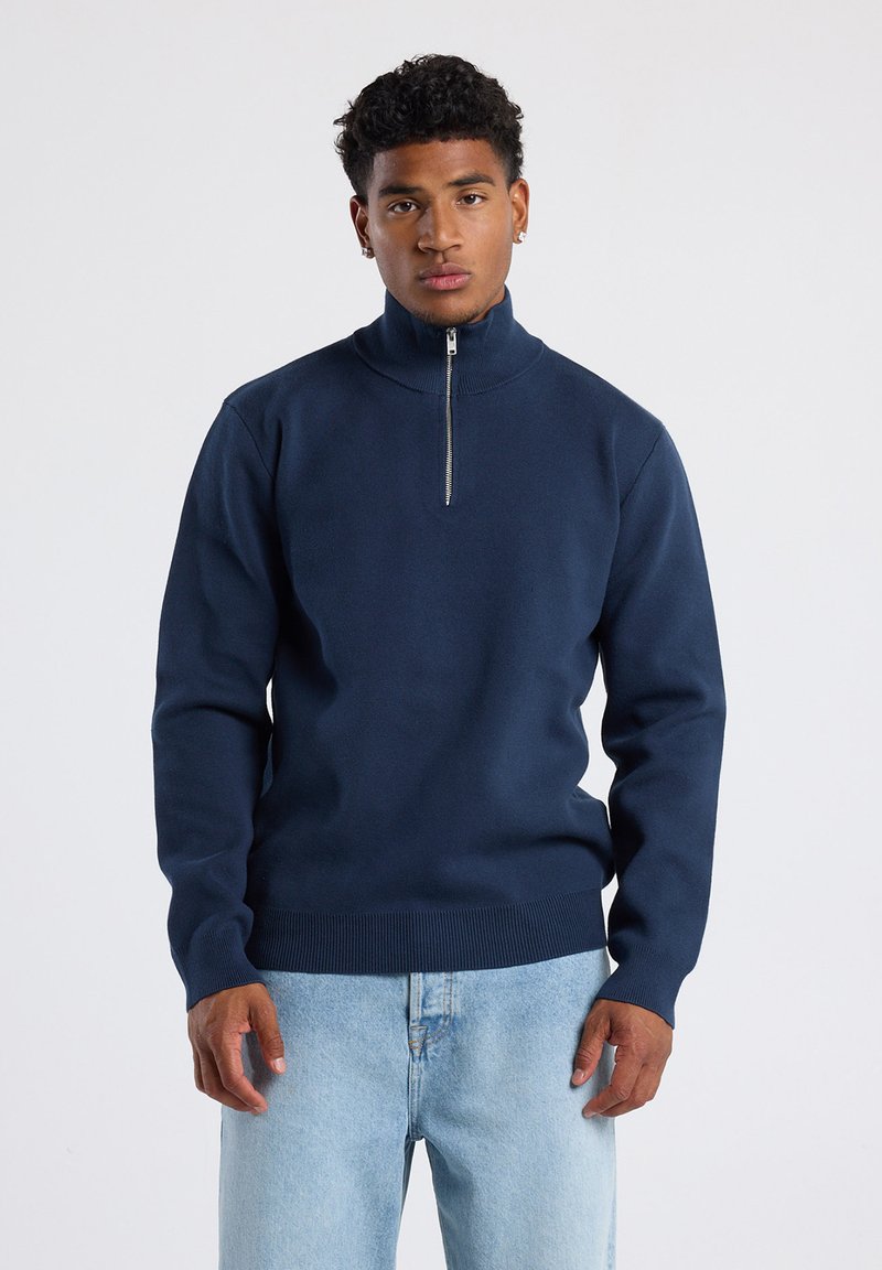 Navy blue zip-neck sweater made of soft fabric, featuring a ribbed hem and cuffs, with a minimalist design and a smooth texture.