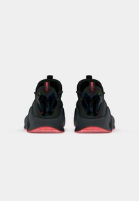 Fekete Nike Free sneaker, textúrált felülettel. Párnázott sarokkal, rózsaszín kiegészítőkkel és minimalista dizájnnal rendelkezik. Hátsó nézetben bemutatva.