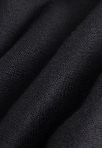 Čierna texturovaná tkanina zobrazujúca jemný pletený vzor s vlnkami a záhybmi, zdôrazňujúc jej hladký a teplý vzhľad.