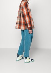 Geruit oranje en zwarte flanellen shirt, gecombineerd met losse blauwe broek en meerkleurige Nike high-top sneakers met witte accenten.