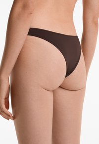 Rjava bikini spodnji del z visokim izrezom, izdelan iz gladkega blaga in z minimalnim šivanjem, ki prikazuje eleganten in sodoben silhuet.