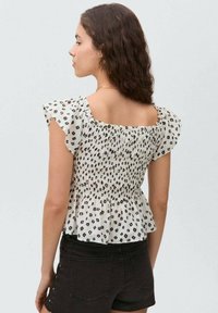 Blusa bianca a maniche corte con corpino arricciato e motivi geometrici neri, con maniche a volantino e orlo peplo.