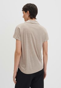 Camicia a maniche corte, con colletto, di un leggero color beige con una texture morbida. Presenta un orlo curvo e una vestibilità comoda, abbinata a pantaloni neri.