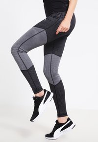 Legginsy z wysokim stanem w kolorze czarnym i szarym, z teksturowanym wzorem. Wyposażone w płaskie szwy i dopasowany krój, zestawione z czarnymi trampkami.