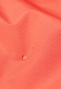 Water droplets resting on textured coral-colored fabric with subtle grid pattern, highlighting water-resistant material properties.