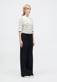 White and black striped polo with short sleeves, paired with black wide-leg trousers. The outfit features a collared neckline and smooth fabric.