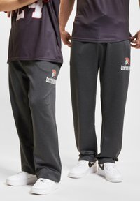 Grå joggebukser med et logo av en spartan-hjelm og teksten "Centurions", laget av mykt stoff med en avslappet passform. Komplementert med hvite sneakers.