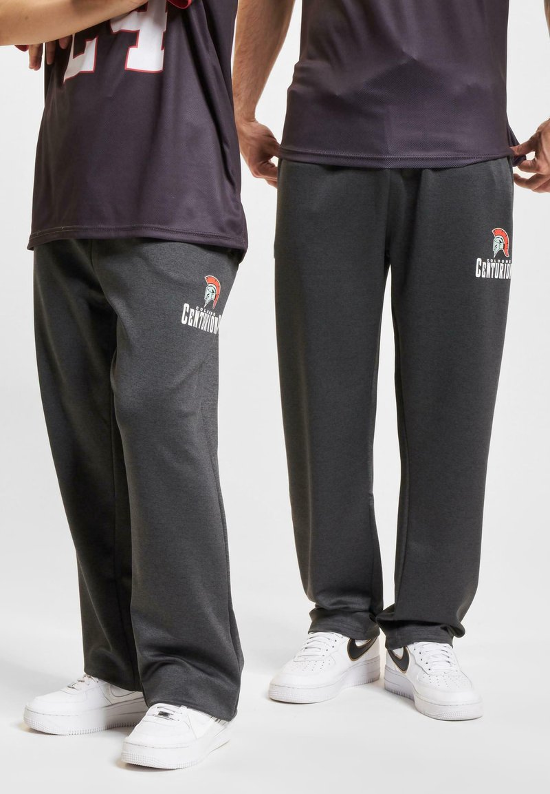 Grå joggebukser med et logo av en spartan-hjelm og teksten "Centurions", laget av mykt stoff med en avslappet passform. Komplementert med hvite sneakers.