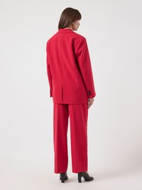 Blazer rouge ajusté avec un col à revers cranté et une fente unique à l'arrière, porté avec un pantalon rouge à jambes larges. Des chaussures à talons noires complètent la tenue.