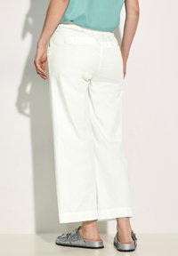 Pantaloni bianchi a gamba larga con vita elastica, texture liscia e spacchi laterali. Abbinati a sandali argentati con dettagli in fibbia.