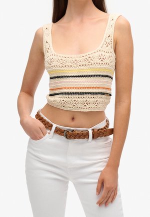 Virkat crop top i krämfärg med färgglada horisontella ränder. Har breda axelband och intrikata spetsmönster. Matchas med vävd brun bälte och vita jeans.