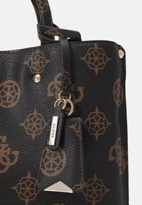 Sort tekstureret håndtaske med brunt geometrisk logomønster. Har guldhardware, et charm-vedhæng med "GUESS" og en struktureret design.