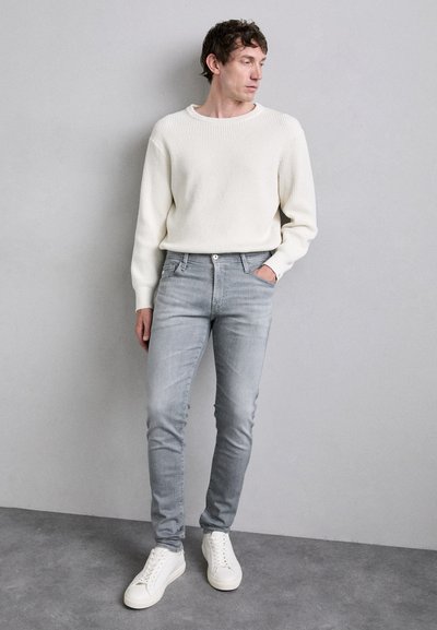Light grey ribbed sweater and fitted light grey jeans, paired with white sneakers. Smooth texture, casual design, and slim silhouette.