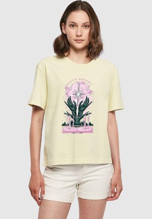 Camiseta de algodón de color amarillo claro con un diseño gráfico de manos y un estallido en rosa, verde y negro, con mangas cortas y un ajuste relajado.