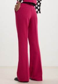 Pantaloni fucsia aderenti a vita alta con design a gamba svasata, caratterizzati da due tasche posteriori e una texture liscia.