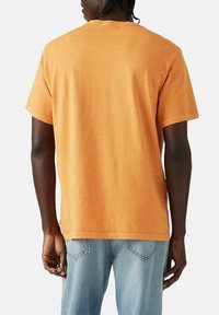Camiseta de manga corta y cuello redondo en algodón naranja. Ajuste relajado con una textura suave, presenta un dobladillo estándar y una silueta clásica.