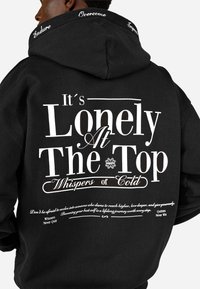 Felpa nera con cappuccio, caratterizzata da un audace testo bianco. La parte posteriore presenta frasi motivazionali e accenti floreali. Realizzata in un morbido misto cotone.