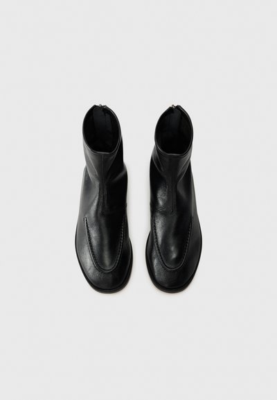 Bottines noires en cuir avec une texture lisse, un design épuré, un bout arrondi et des zips latéraux pour un enfilage facile.